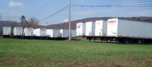 A line of white ALLEN branded storage trailers parked in a field with green grass, under a clear sky with hills in the background.