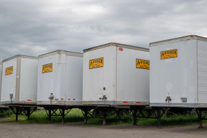 A row of white A-Verdi storage trailers parked on a gravel lot under an overcast sky.