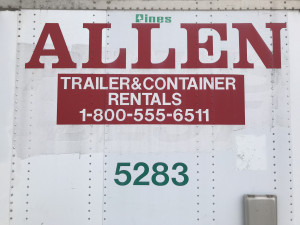 Close-up of a white surface with "ALLEN TRAILER & CONTAINER RENTALS" and a phone number in red lettering, with the number "5283" below.